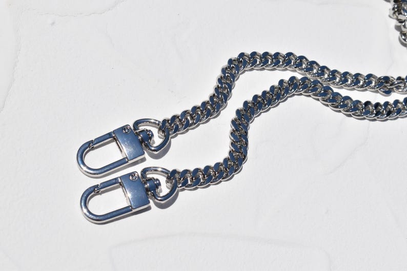 a pair of silver metal chain straps with lock-like attachments, lying on a white surface.