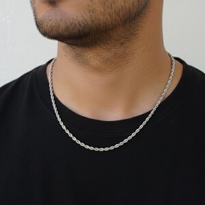 A close-up of a man wearing a silver chain necklace against a black shirt.