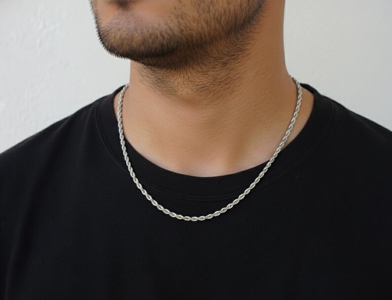 A close-up of a man wearing a silver chain necklace against a black shirt.