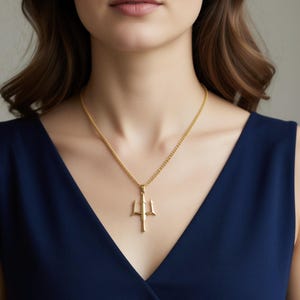 A woman wearing a gold necklace with a pendant is shown in the image.