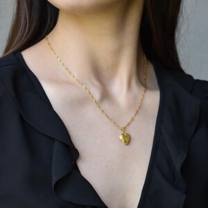 A close-up of a woman wearing a black blouse with a gold heart-shaped pendant necklace.