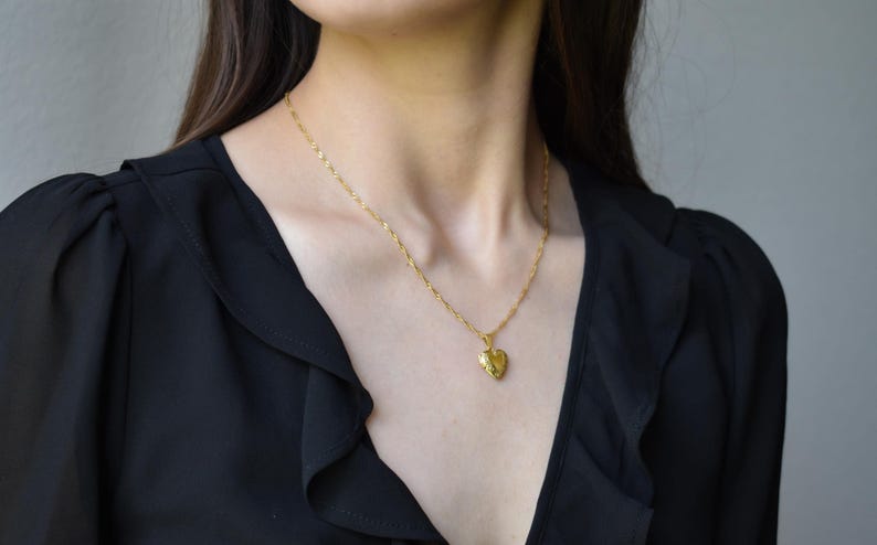 A close-up of a woman wearing a black blouse with a gold heart-shaped pendant necklace.