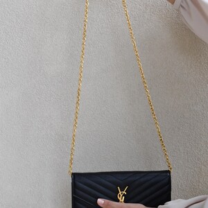 A person's hand holding a black Yves Saint Laurent wallet with a gold chain strap.