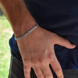 A close-up view of a person's hand wearing a silver bracelet, with a blurred background of grass.