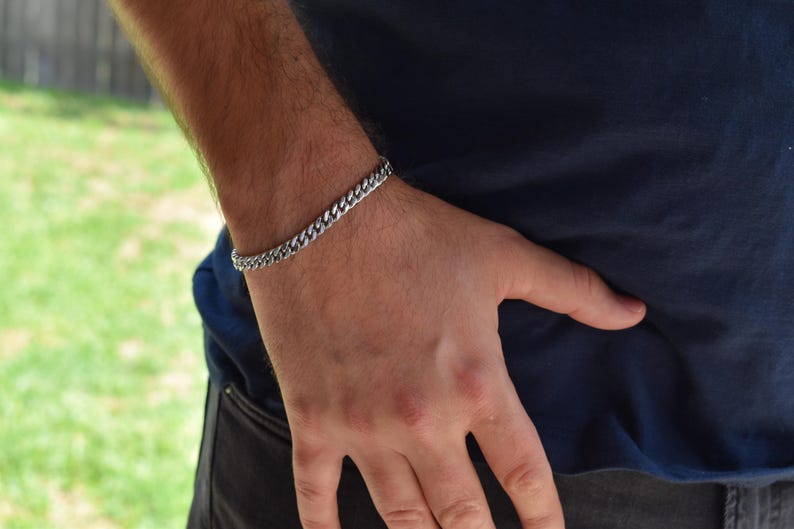 A close-up view of a person's hand wearing a silver bracelet, with a blurred background of grass.