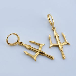 two gold-colored earrings with a trident design, placed on a light blue background.