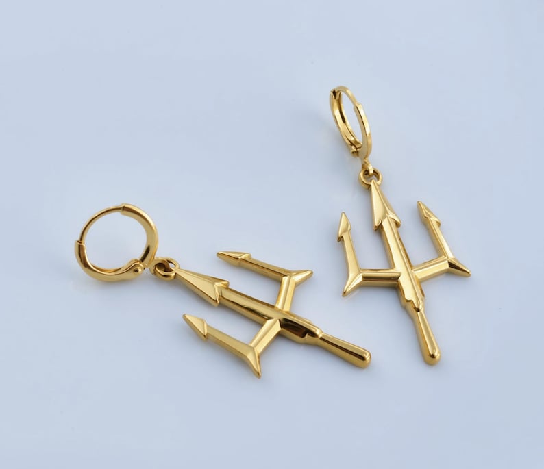 two gold-colored earrings with a trident design, placed on a light blue background.