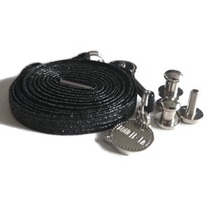May include: A black shoelace kit with silver-toned hardware. The kit includes a coiled flat shoelace, metal rivets, and a charm with the text "FOUR II - 16". The items are arranged on a white surface.
