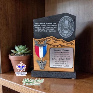 May include: A personalized Eagle Scout award plaque with a black stone base and a wooden top. The plaque features a medal, the BSA logo, and the text "TAKE PRIDE IN HOW FAR YOU'VE COME..." and "EAGLE SCOUT". A small potted succulent is next to the plaque.