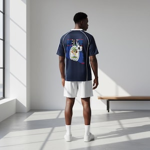 May include: Navy blue soccer jersey with white trim and the word "BELIZE" above a Belize flag and soccer ball graphic. The person is also wearing white shorts and white socks.