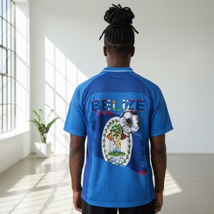 May include: Blue soccer jersey with the word "BELIZE" across the back. The jersey features the Belize flag and a soccer ball graphic. The shirt has short sleeves and a ribbed collar.