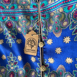 May include: A blue fabric with a paisley pattern and gold stars. The fabric has a gold trim and a brown tag that says "Purple Desert Vintage".