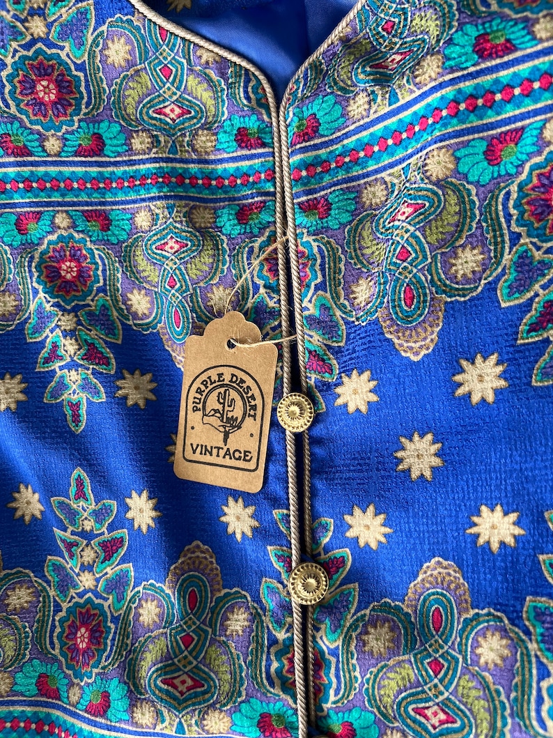 May include: A blue fabric with a paisley pattern and gold stars. The fabric has a gold trim and a brown tag that says "Purple Desert Vintage".