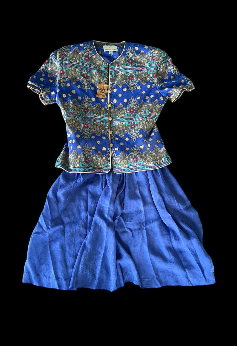 May include: A blue and gold patterned blouse with short sleeves and a matching blue skirt. The blouse has a button-up front and a small tag that says "Country Road".