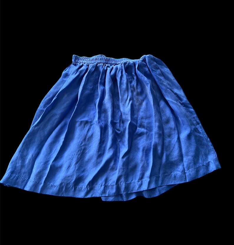 May include: A blue skirt with a gathered waistband. The skirt is made of a soft, lightweight fabric.