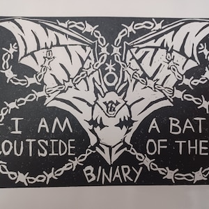 May include: Black and white linocut print of a bat with wings spread wide. The bat is surrounded by barbed wire and the text "I am outside of the binary" is printed below.