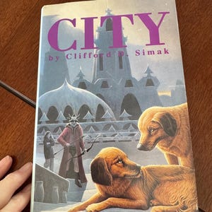May include: A paperback book titled "CITY" by Clifford D. Simak. The cover art features a fantasy scene with a castle, figures, and two dogs. The title is in purple, and the background is a cool color palette.