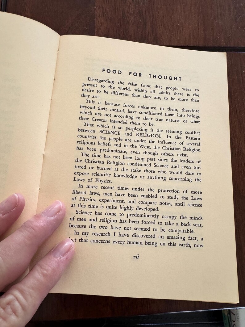 May include: Open book page with the title "FOOD FOR THOUGHT" and text discussing the conflict between science and religion. The page is yellowed with age, and the text is in black. A hand is visible.