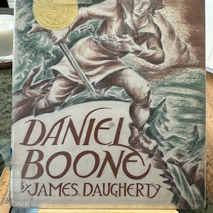 May include: A vintage book cover with a drawing of a man holding a rifle, running through the woods. The title of the book is "Daniel Boone" by James Daugherty.