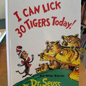 May include: A hardcover book titled "I Can Lick 30 Tigers Today!" by Dr. Seuss. The cover features a cartoon illustration of the Cat in the Hat and several tigers. The title is in red, and the author's name is in green.