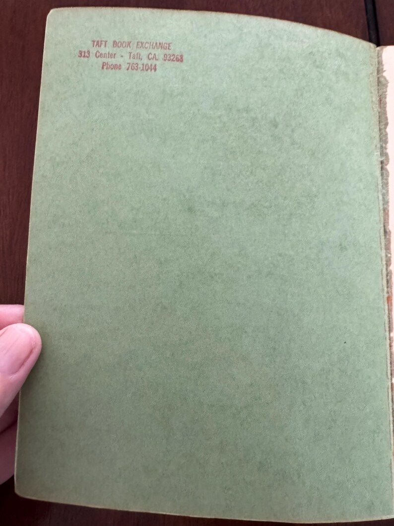 May include: Open book with a light green cover. The text "TAFT BOOK EXCHANGE" is printed in red at the top, along with the address and phone number. The book's pages are visible on the right side.
