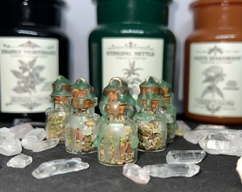 May include: Five small glass bottles with cork stoppers and green wax seals. The bottles are filled with dried herbs and crystals. The bottles are sitting on a black surface with clear quartz crystals.