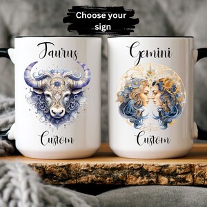 May include: Two white ceramic mugs with black handles. The mug on the left features a blue and gold illustration of a bull with the word "Taurus" and "Custom" written below. The mug on the right features a blue and gold illustration of two women's faces with the word "Gemini" and "Custom" written below. The text "Choose your sign" is written in black on a white background above the mugs.