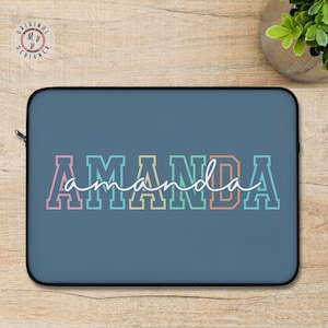 May include: A blue laptop sleeve with the name "AMANDA" in colorful block letters. The name is outlined in white, with a cursive "amanda" overlay. The sleeve has a black zipper and a black border.