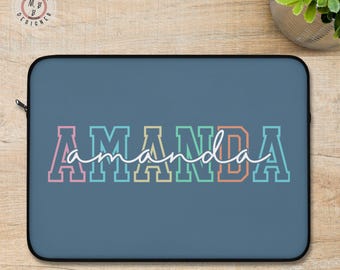 May include: A blue laptop sleeve with the name "AMANDA" in colorful block letters. The name is outlined in white, with a cursive "amanda" overlay. The sleeve has a black zipper and a black border.