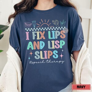 May include: Navy blue t-shirt with the text "I FIX LIPS AND LISP SLIPS" in colorful letters. The shirt features speech therapy-related graphics and the hashtag #speech therapy.