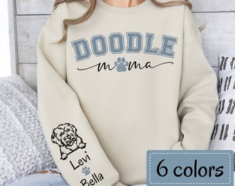 May include: A beige sweatshirt with the text "Doodle mama" in blue with a paw print. The left sleeve has a doodle dog illustration with the names "Levi" and "Bella" underneath.