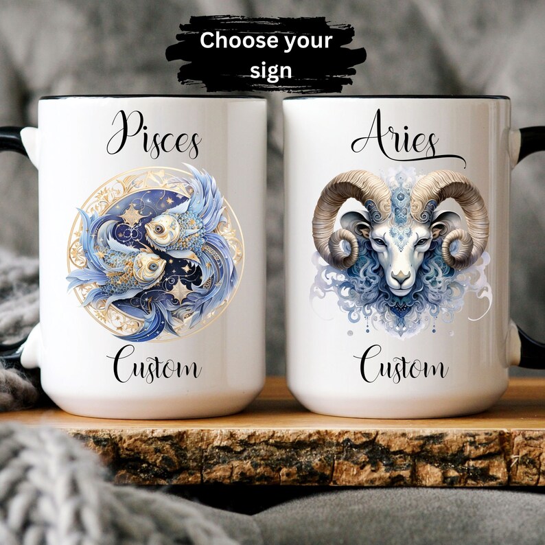 May include: Two white ceramic mugs with black handles. The mug on the left features a blue and gold illustration of two fish with the word "Pisces" above and "Custom" below. The mug on the right features a blue and gold illustration of a ram's head with the word "Aries" above and "Custom" below. The text "Choose your sign" is visible above the mugs.