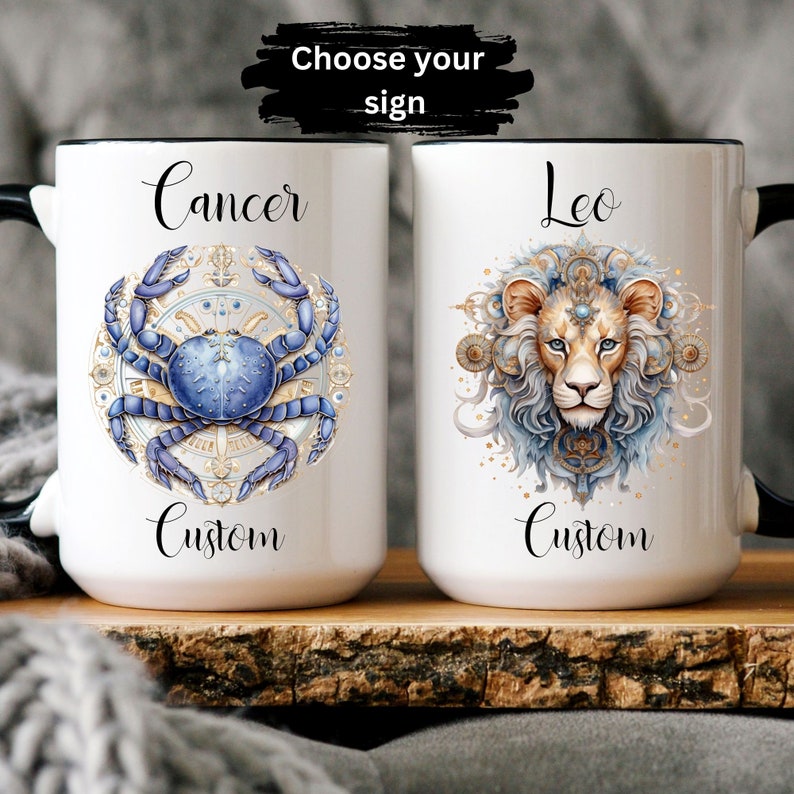 May include: Two white ceramic mugs with black handles. The mug on the left features a blue and gold illustration of a crab with the word "Cancer" above it and "Custom" below it. The mug on the right features a blue and gold illustration of a lion with the word "Leo" above it and "Custom" below it.