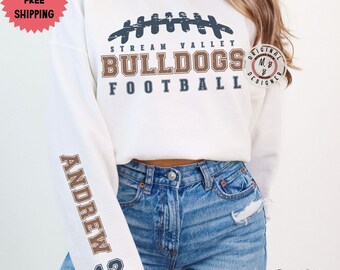 May include: White sweatshirt with a football design and the text "Stream Valley Bulldogs Football". The sleeve has the text "Andrew 12" in brown and blue.