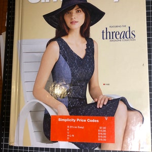 May include: A magazine cover for Simplicity featuring a woman wearing a black hat and a blue and black dress. The magazine cover features the text "Simplicity" and "threads magazine collection".