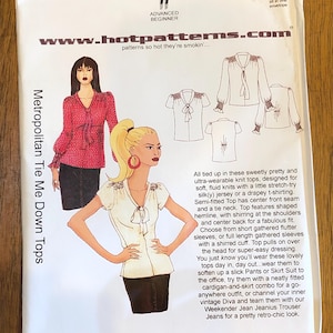 May include: A sewing pattern envelope for "Metropolitan Tie Me Down Tops" by Hot Patterns. The envelope features illustrations of the tops, skill level, and sizing information. The design includes tie necks, shaped hemlines, and various sleeve options.