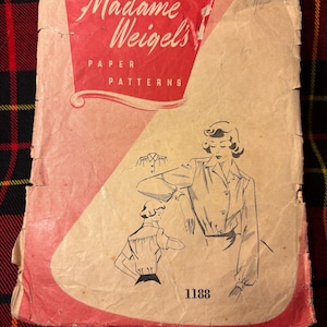 May include: A vintage Madame Weigel's paper patterns envelope with a red and tan color scheme. The front features a black line drawing of a button-down shirt with long sleeves and the number 1188. The paper is worn with visible creases and edges.
