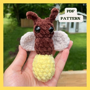 May include: A crocheted firefly amigurumi toy with brown and white fur, yellow yarn for the light, and black eyes. The toy is being held in a hand. The text "PDF PATTERN" is visible in the background.
