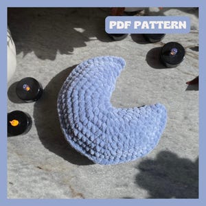 May include: A light blue crescent moon shaped pillow with a textured surface. The pillow is made of a soft, fluffy material.