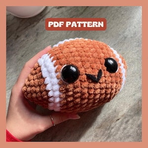 Könnte beinhalten: Gehäkeltes Plüsch-Fußballspielzeug mit braunem und weißem Farbmuster und einem niedlichen Comic-Gesicht. Das Spielzeug hat große schwarze Augen und eine kleine schwarze Nase.