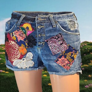 May include: Blue denim shorts featuring a button-fly closure and the Universal Thread brand label. The shorts are decorated with various colorful fabric patches, including floral, paisley, and metallic silver butterfly-shaped appliqués.