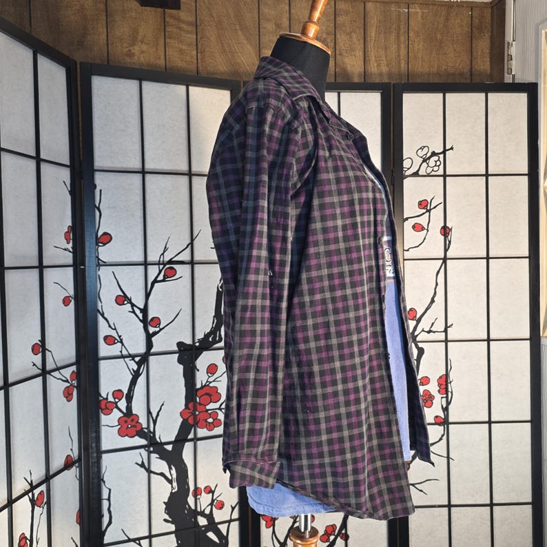 May include: A long-sleeved button-down shirt featuring a dark purple and charcoal gray plaid pattern. The shirt is displayed on a mannequin torso and includes a classic collar, a front button placket, and buttoned cuffs on the sleeves.