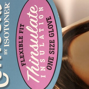Op de afbeelding: Een close-up van een productlabel met de tekst "Flexible Fit Thinsulate Insulation One Size Glove" in wit en roze op een blauwe achtergrond. De merknaam "Contours by Isotoner" is ook zichtbaar.