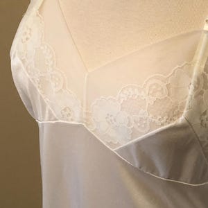 May include: Cream-coloured lingerie with delicate lace detailing. The slip features a satin-like fabric and a sheer panel at the neckline, adorned with floral lace. The straps are thin and adjustable.