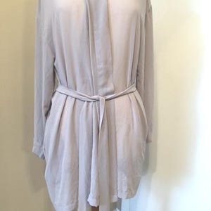 May include: A light gray robe with long sleeves and a matching belt tied at the waist. The robe has a draped neckline and a flowing, relaxed fit. The fabric appears soft and lightweight, suitable for lounging or layering.