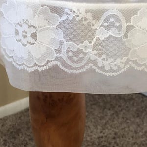 May include: A close-up view of a white slip, showcasing a detailed floral lace trim. The lace design includes repeating floral motifs and a scalloped border. The fabric is a soft, semi-transparent material.