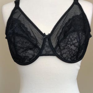 May include: A black underwire bra featuring sheer mesh fabric with a subtle dotted pattern on the upper cups and intricate floral lace detailing on the lower sections. The garment includes adjustable shoulder straps and a small center bow.
