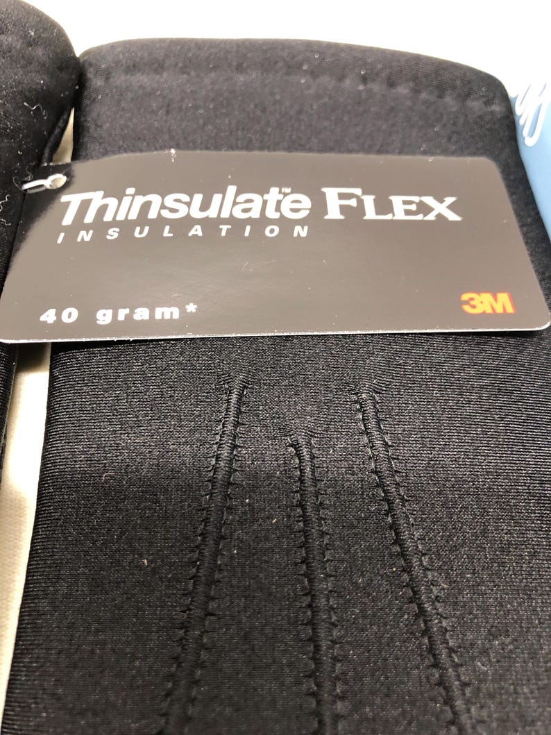 Op de afbeelding: Zwarte handschoenen met een label met de tekst "Thinsulate FLEX INSULATION" en "40 gram*". De handschoenen zijn gemaakt van een glad, donker materiaal en hebben zichtbare stiksels. Het 3M-logo is ook zichtbaar op het label.