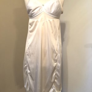 May include: Ivory-colored slip dress with adjustable straps and a delicate lace trim at the hem. The bodice features a subtle decorative element. The dress is displayed on a mannequin.