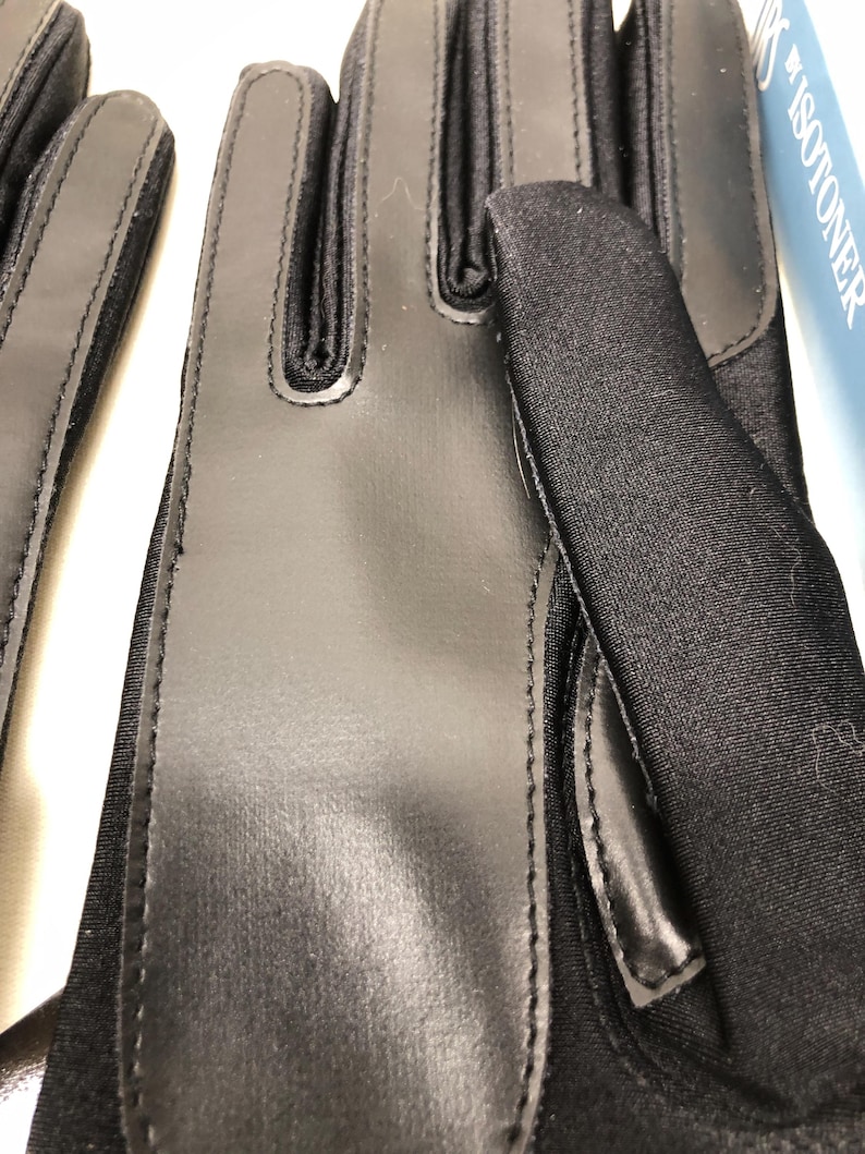 Op de afbeelding: Close-up van zwarte handschoenen met een combinatie van glad, glanzend materiaal en textuurstof. De handschoenen hebben een strak ontwerp met gestikte naden en verstevigde zones. De merknaam "ISOTONER" is gedeeltelijk zichtbaar op de achtergrond.